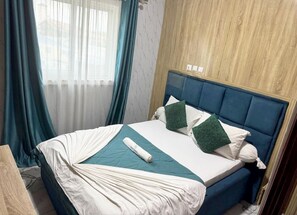 Una cama bien hecha con cabecera azul, ropa de cama blanca y un detalle en color verde azulado.