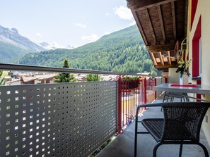 Ein Balkon mit Blick auf eine Berglandschaft, einem Tisch mit Stühlen und einem roten Geländer.