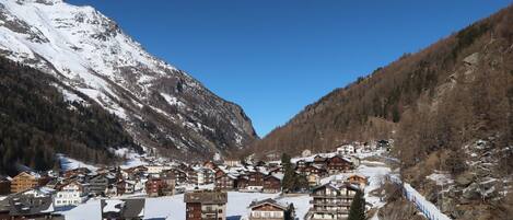 A snow-covered mountain village with traditional wooden buildings, a clear sky, and a ski slope.
