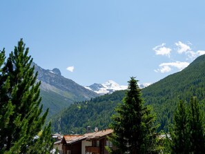 Eine Berglandschaft mit einem Haus im Vordergrund und schneebedeckten Gipfeln im Hintergrund.