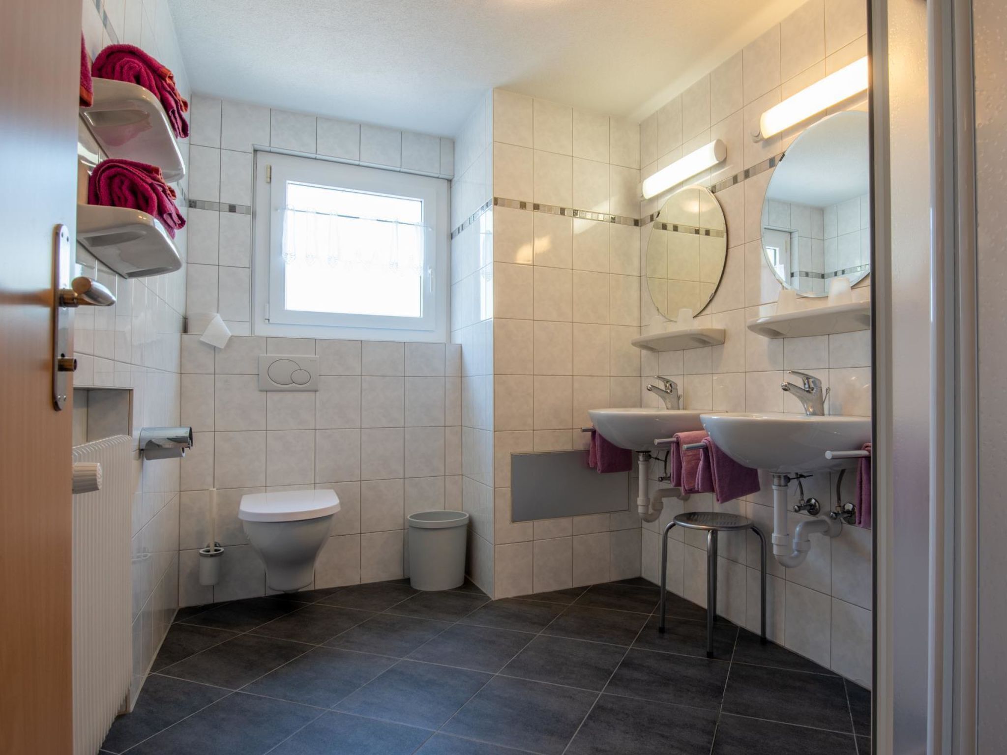 Uma casa de banho moderna com sanita, duas pias, espelho e janela.