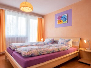 Ein Schlafzimmer mit einem Bett, zwei Nachttischlampen, einem Fenster mit Vorhängen und einem Bild an der Wand.