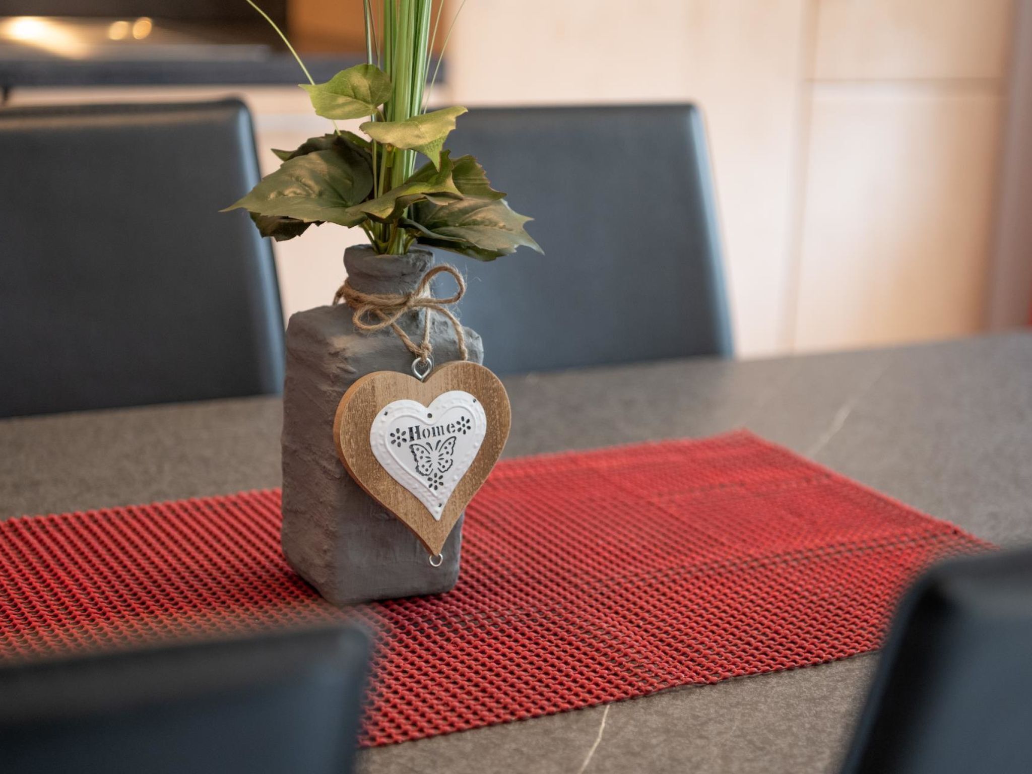 Ein Tisch mit einer Vase, darin eine Pflanze und ein herzförmiges Schild mit dem Wort 'Home'.