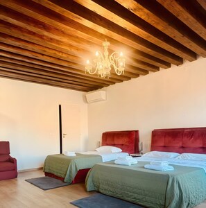Een hotelkamer met twee bedden, een rood bekleden hoofdeinde, een kroonluchter en een houten plafond.