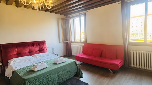 A room with a bed, a red sofa, a chandelier, and large windows. - Room 'Ca Pisani Su Canal Grande Azzuro' with Wi-Fi (Venice)