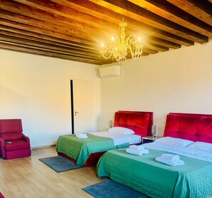 Ein Hotelzimmer mit zwei Betten, einem roten, gepolsterten Kopfteil, einer Kristallleuchtre und einem roten Sessel.