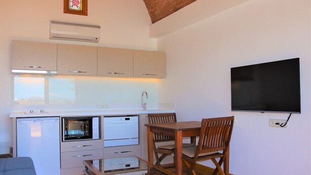 A compact kitchen with a built-in oven, a dishwasher, and a dining area with a table and chairs. - Munahan Hotel Bodrum (Bodrum)
