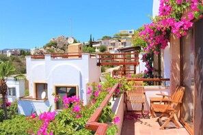 A balcony with wooden furniture and pink flowers, overlooking a residential area.
