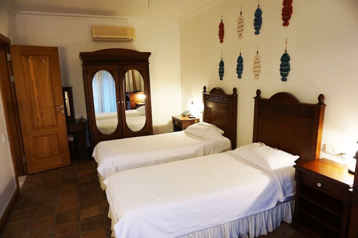 A hotel room with two beds, a wardrobe, a mirror, a bedside table, and wall decorations.