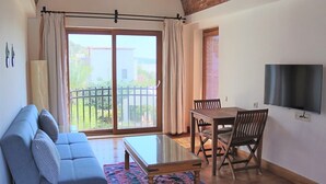 A living room with a sofa, a glass coffee table, a dining table with chairs, a TV mounted on the wall, and a sliding glass door leading to an outdoor area. - Munahan Hotel Bodrum (Bodrum)