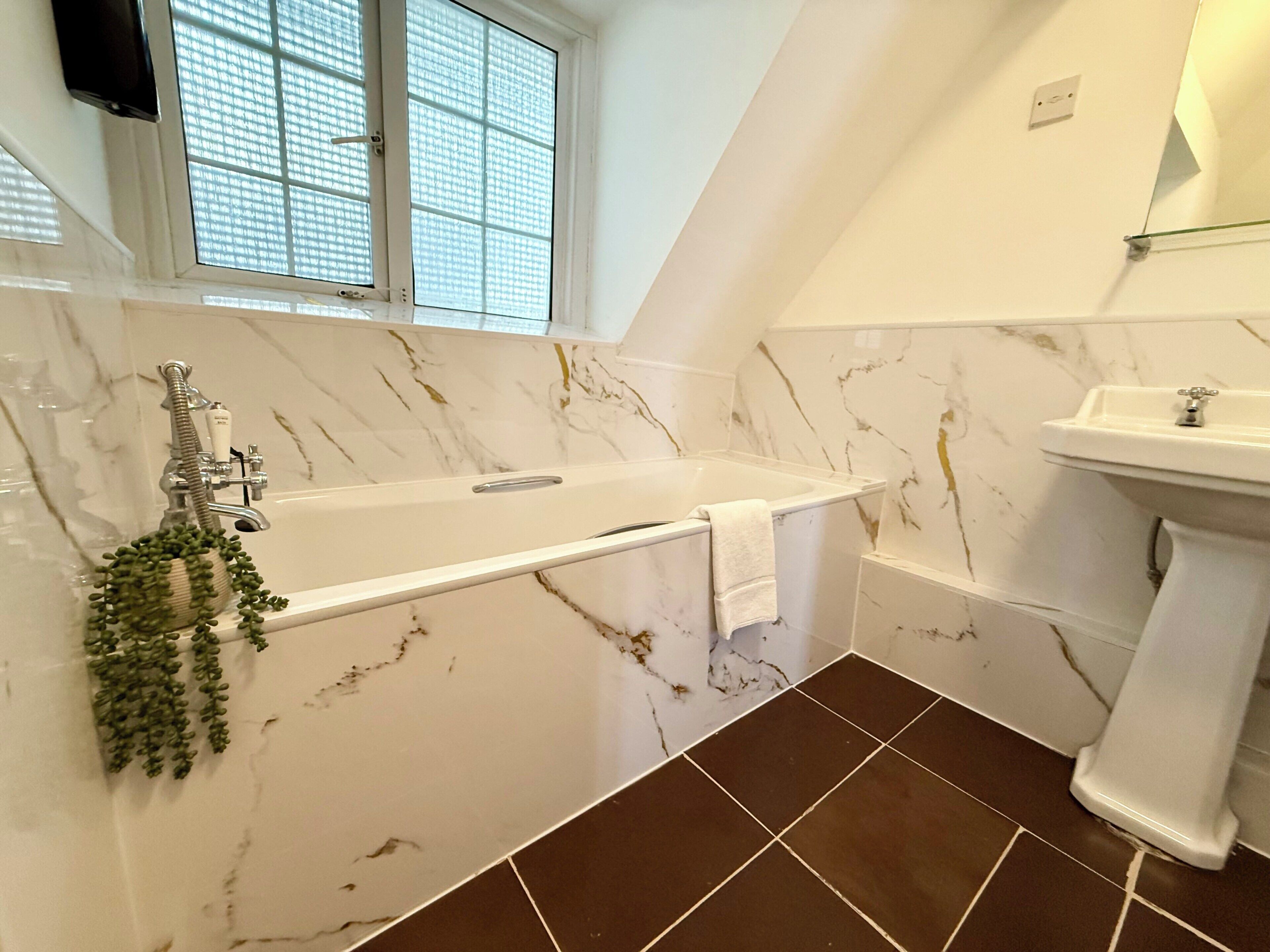 A bathroom with a bathtub, a sink, and a window with blinds.