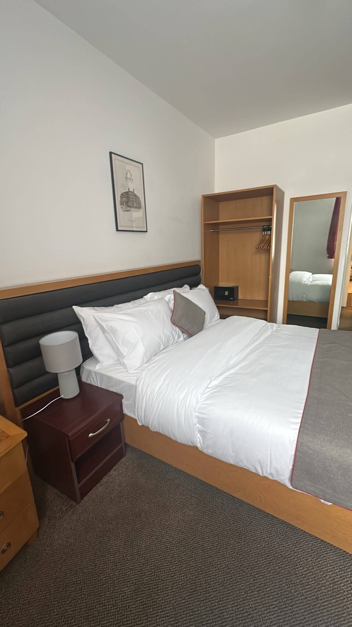 Une chambre d’hôtel comprenant un lit, une table de chevet, une lampe, une armoire et un miroir.