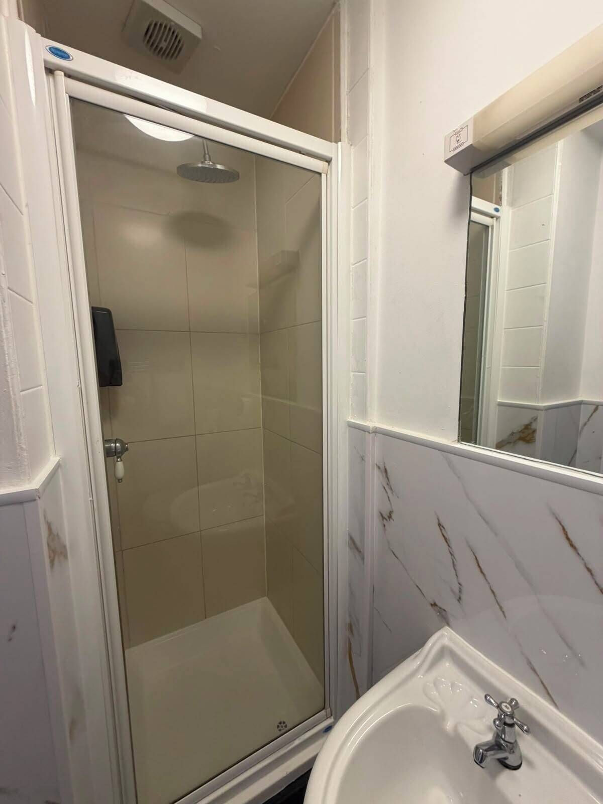 Een badkamer met een douche met glazen wanden, een wastafel met één kraan en een spiegel boven de wastafel.