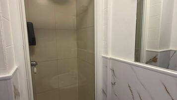 Een badkamer met een douche met glazen wanden, een wastafel met één kraan en een spiegel boven de wastafel.