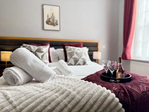 A hotel room with a neatly made bed, a bottle of wine, and glasses on a tray.