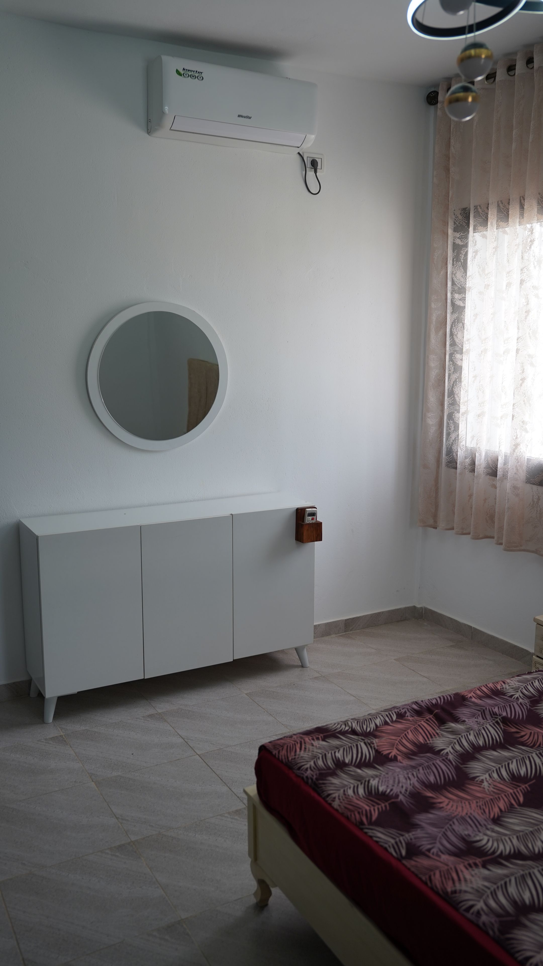 Un dormitorio con cama, mesita de noche, espejo, armario y ventana con cortinas.