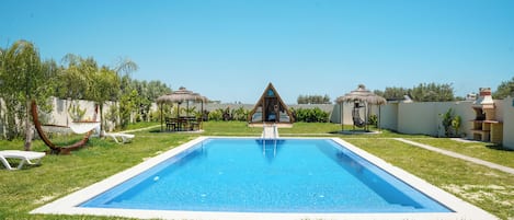 Una piscina con una plataforma de observación triangular, rodeada de césped y árboles.
