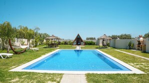 Una piscina con una plataforma de observación triangular, rodeada de césped y árboles.