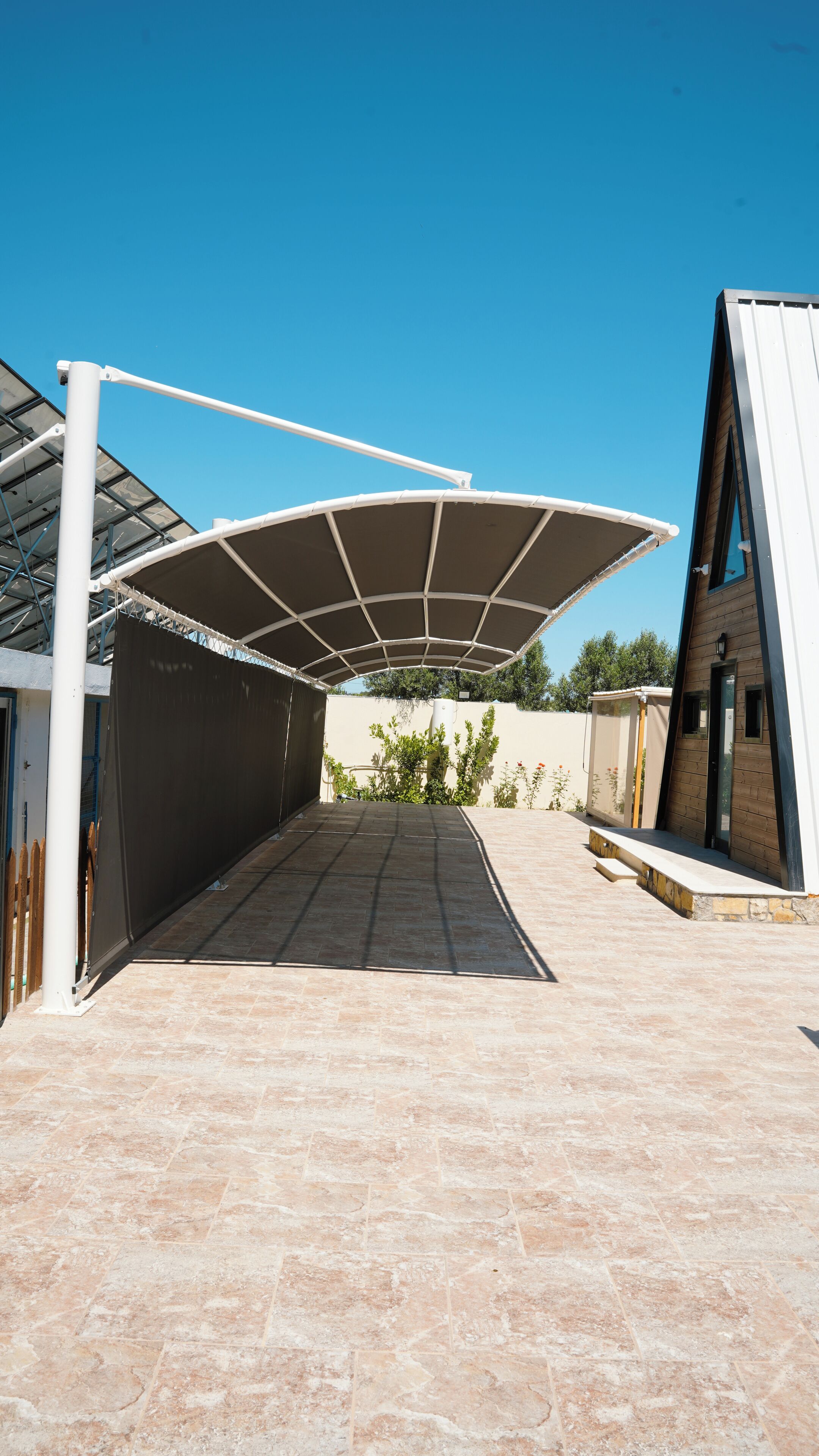 A covered outdoor area with a tiled floor, a white structure on the left, and a building with a sloped roof on the right.
