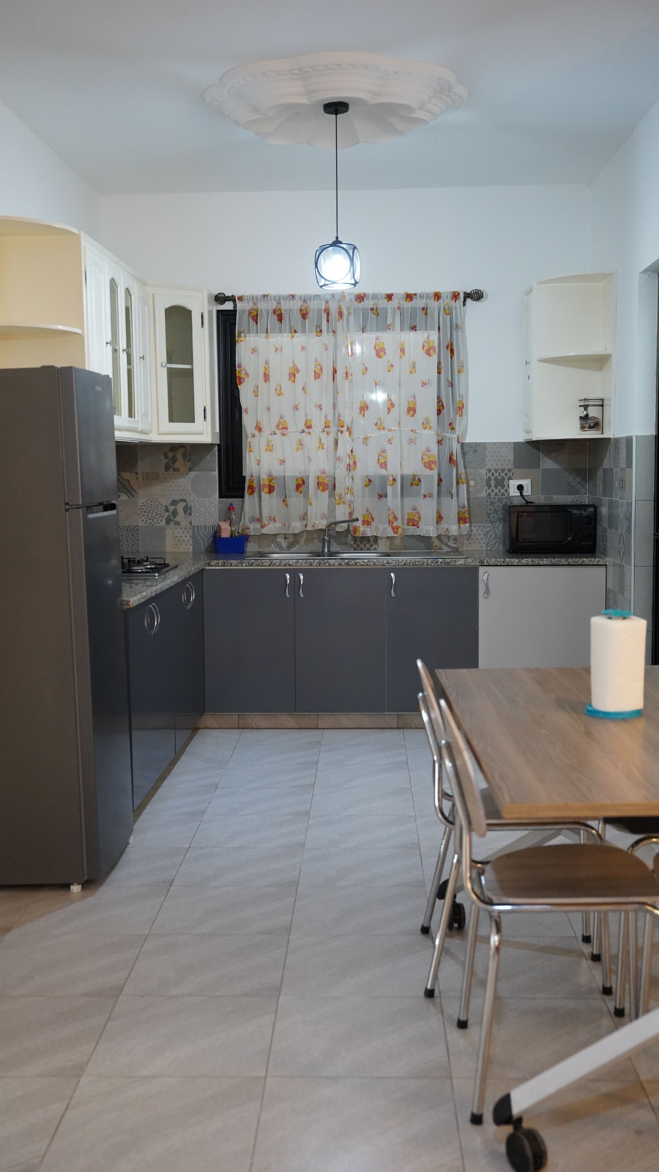 Una cocina con refrigerador, microondas y una mesa de comedor con sillas.