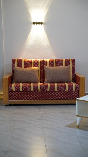Un canapé recouvert d’un tissu à motifs, agrémenté de deux coussins, placé contre un mur où se trouve un luminaire.