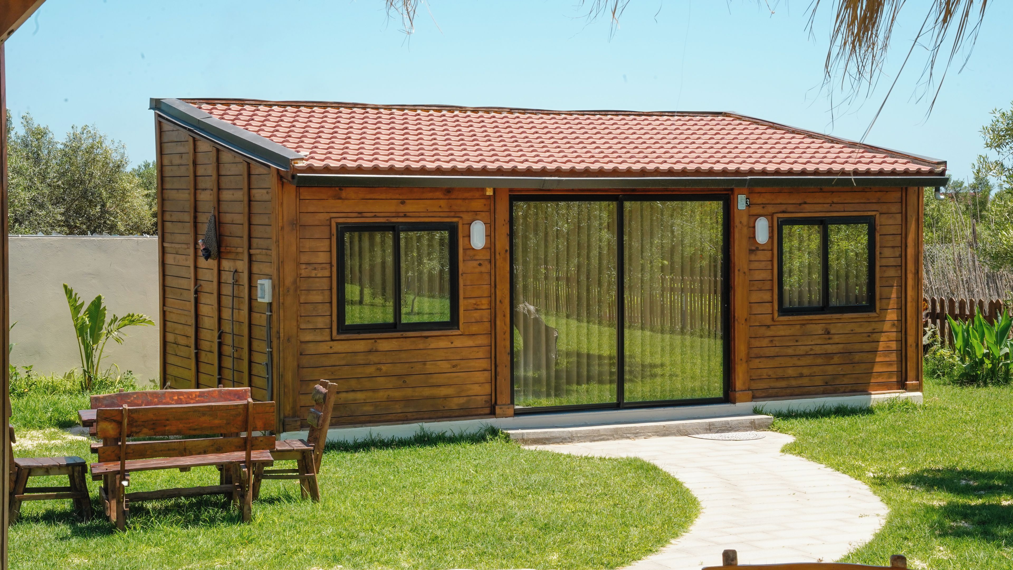 Eine Holzhütte mit Ziegeldach, großen Schiebeglastüren und einer Bank im Garten.