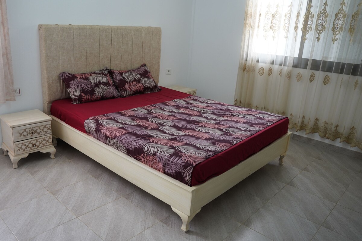 Une chambre à coucher avec un lit, une table de chevet et une fenêtre avec des rideaux.