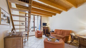 Ein gemütliches Wohnzimmer mit Holzbalkendecke, einer Couch, einem Couchtisch und einem Fernseher.