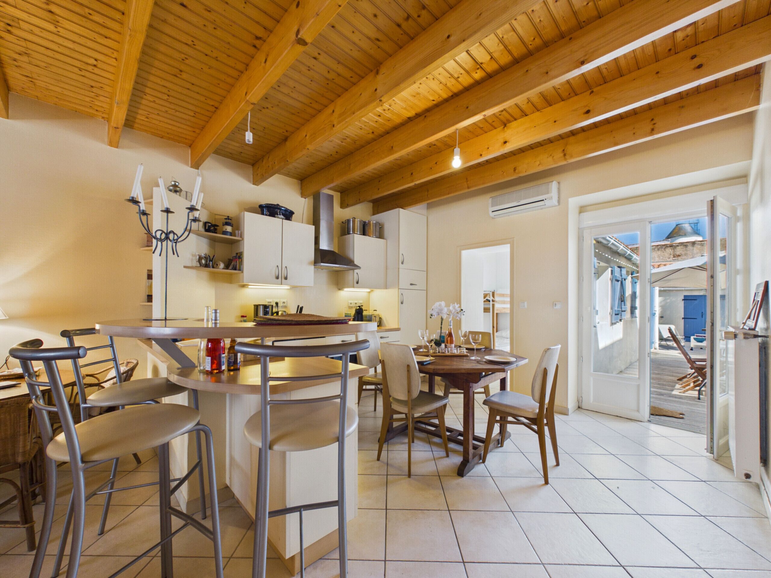 A modern kitchen with wooden beams, a bar area, and a dining space with chairs and tables.