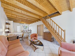 Uma sala de estar ampla com teto de madeira alto, uma escadaria e um espaço de jantar com cadeiras e uma mesa.