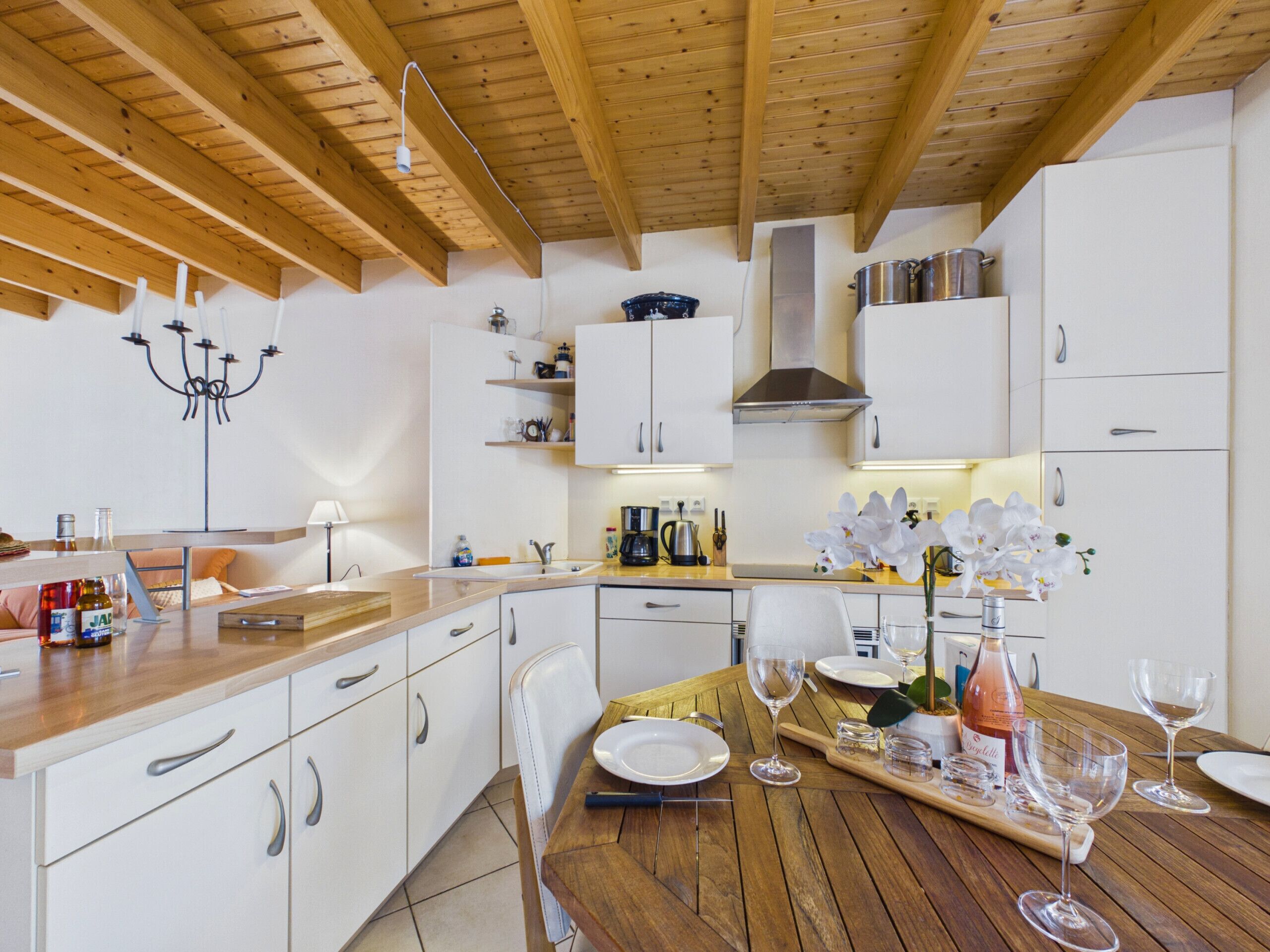 Une cuisine moderne avec des poutres en bois, des meubles blancs et un coin repas aménagé pour prendre un repas.