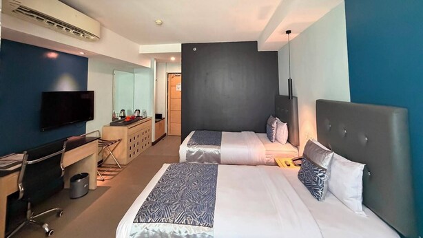 Ein Hotelzimmer mit zwei Betten, einem Schreibtisch, einem Sessel, einem Fernseher und einem Kleiderschrank.