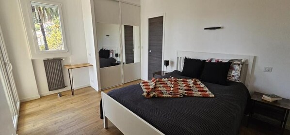 A bedroom with a bed, a bedside table, a mirror, a radiator, and a window. - Cannes Sea View Beach Private Room (Cannes)