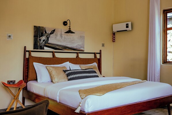 A neatly made bed with a wooden headboard, a wall-mounted air conditioner, and a painting of a horse's head.