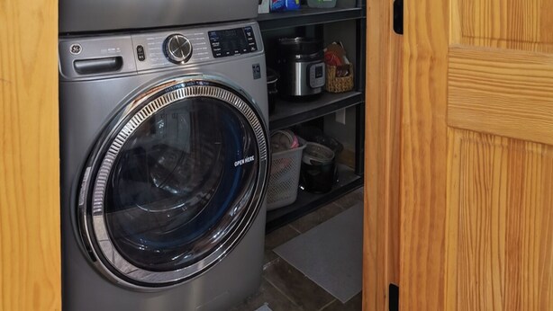 Un lavadero con dos lavadoras apiladas de carga frontal, una puerta de madera y un estante con productos de limpieza.