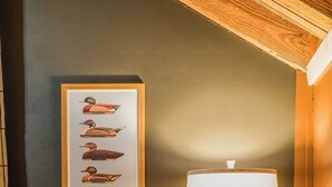 Un dormitorio con cama, mesita de noche con lámpara, un cuadro en la pared y un enchufe.