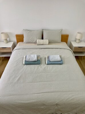 Ein ordentlich gemachtes Bett mit gestreifter Bettwäsche, zwei Kissen und gefalteten Handtüchern auf einem weißen Nachttisch.
