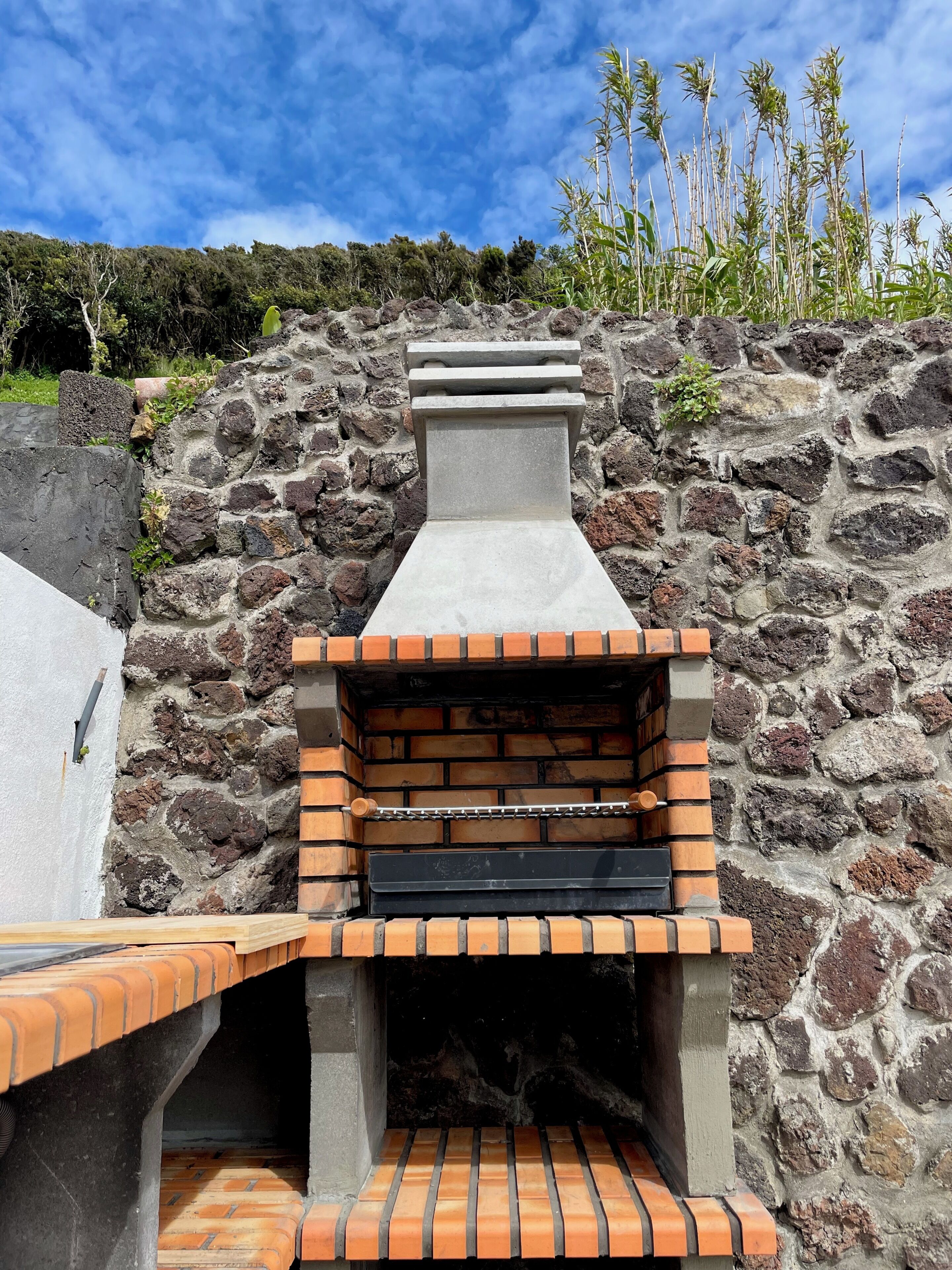 A brick-built outdoor oven with a stone wall backdrop.