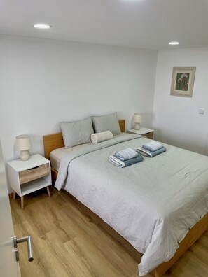 Un dormitorio ordenado con cama, dos mesitas de noche y una lámpara de pared.