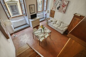 A dining area with a glass table set for four, a sofa, and a television in a corner. - Via Maggio 10 – Historic Loft in Oltrarno  (Florence)