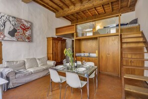 A dining area with a glass table, white chairs, and a wooden staircase. - Via Maggio 10 – Historic Loft in Oltrarno  (Florence)