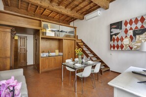 A dining area with a glass table, white chairs, and a vase of sunflowers. - Via Maggio 10 – Historic Loft in Oltrarno  (Florence)