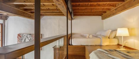 Una habitación con techo de madera, una cama con ropa de cama blanca, una mesita de noche con lámpara y una ventana con vistas.