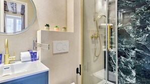 A bathroom with a marble shower, a white sink, and a mirror with a round frame. - Charming Apartment in Le Marais Center of Paris (Paris)