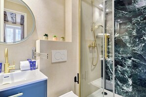Ein Badezimmer mit einer Marmordusche, einem weißen Waschbecken und einem Spiegel mit runder Rahmung.