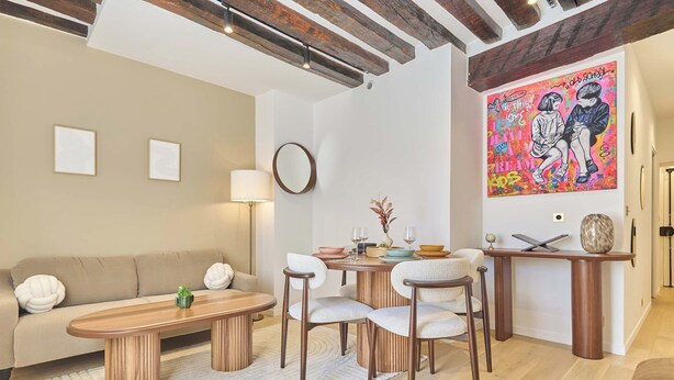A modern living room with a sofa, coffee table, and chairs, a dining area with a table set for two, and a colorful artwork on the wall. - Charming Apartment in Le Marais Center of Paris (Paris)
