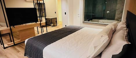 Un dormitorio moderno con cama, televisión, escritorio y un amplio ventanal.