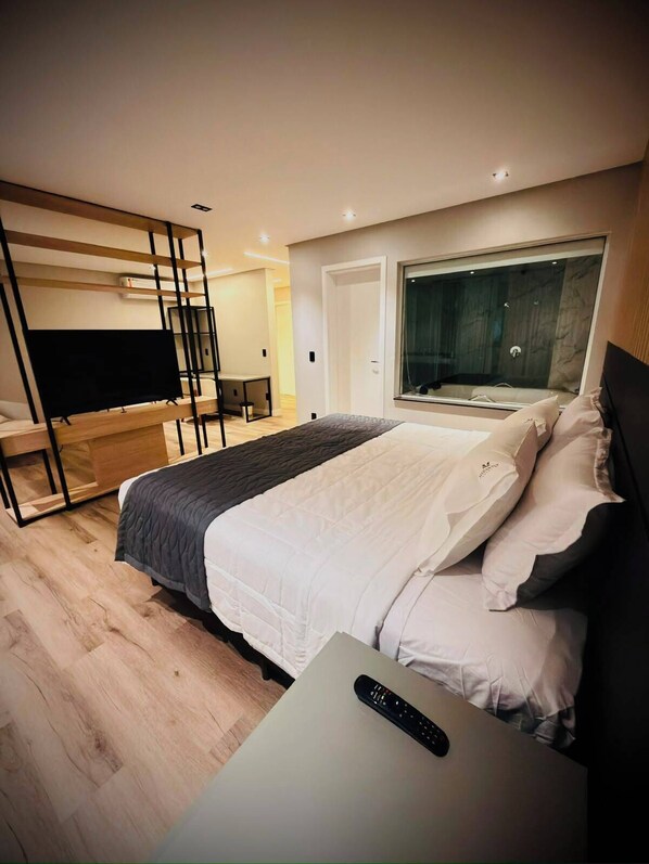 A modern bedroom with a bed, a TV, a desk, and a large window.