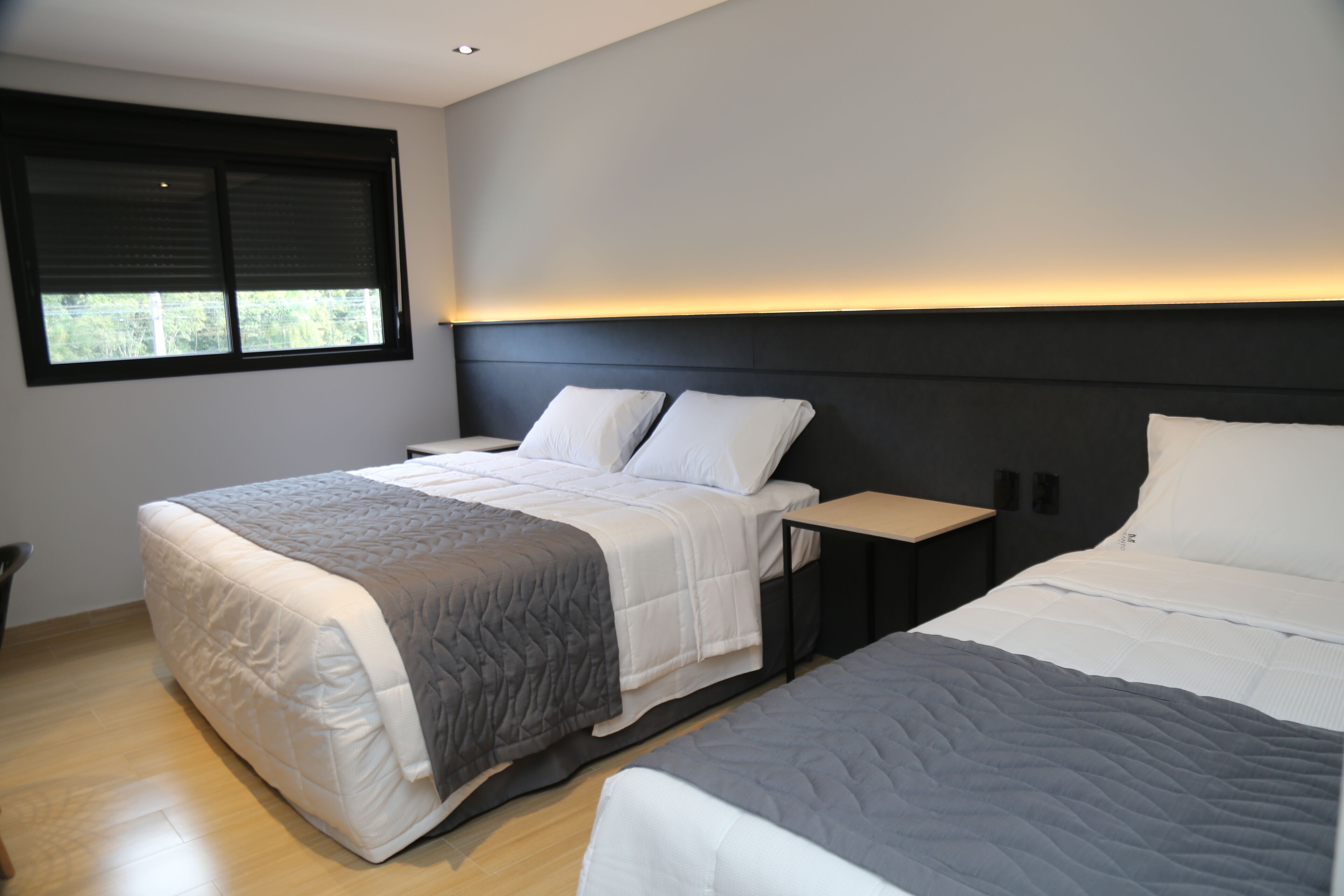 Een moderne slaapkamer met een groot bed, een kleiner bed, een nachtkastje en een raam met jaloezieën.