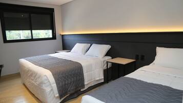 A modern bedroom with a large bed, a smaller bed, a nightstand, and a window with blinds.